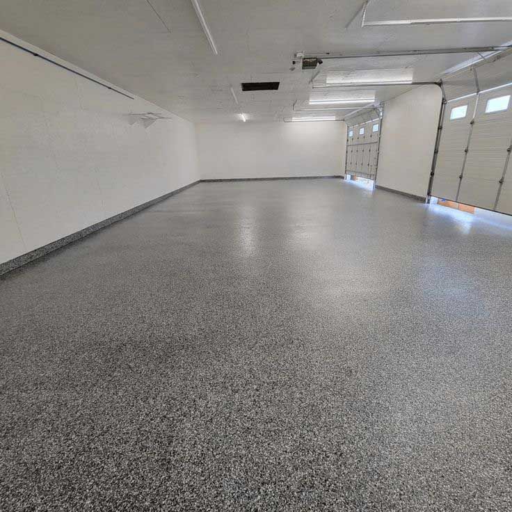 Empty, clean garage with gray epoxy flooring. White walls, open garage doors.
