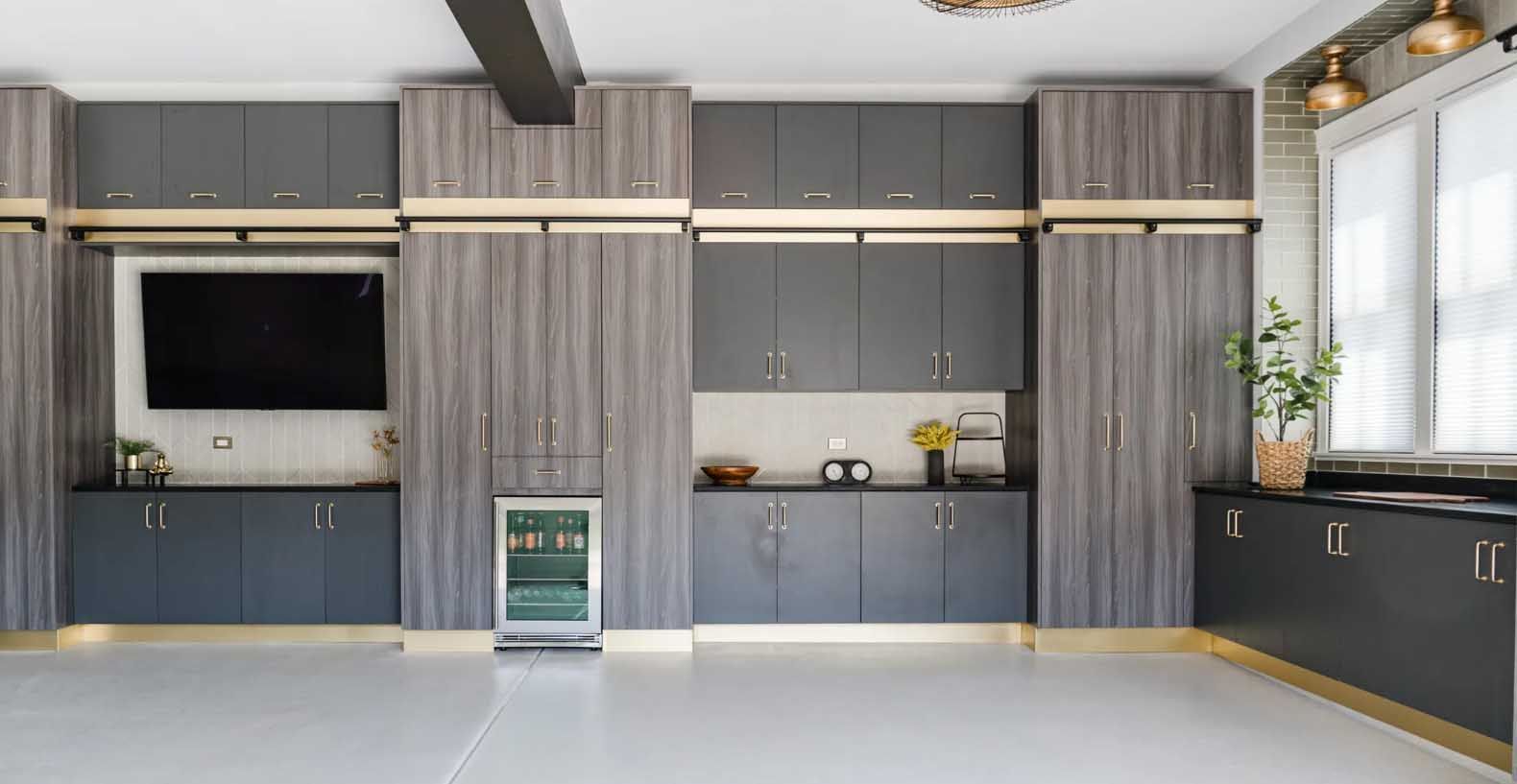 Modern garage with gray and wood cabinets, TV, small fridge, and white floor.