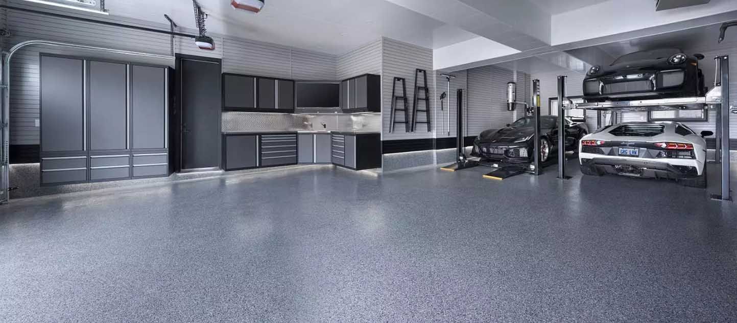 Clean garage with cabinets, vehicles on lifts, and a stylish grey floor.