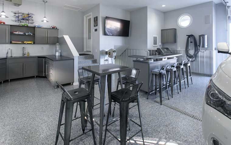 Spacious, modern garage with kitchen, bar, seating, and car. Grey cabinets and flooring.