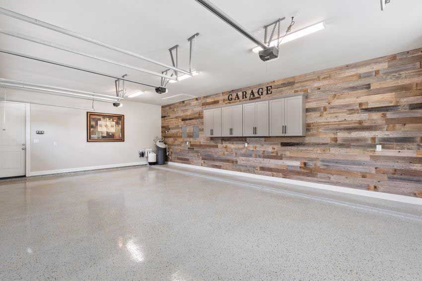 Spacious, empty garage with a wood accent wall, cabinets, and a polished concrete floor.