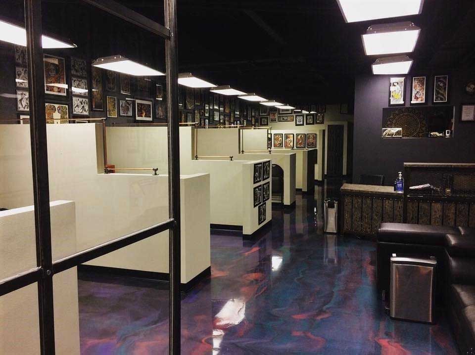Interior of a tattoo parlor with white cubicles, glossy purple floor, and framed art on the walls.