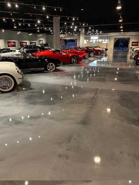 Cars in a showroom with polished, reflective gray floor. Black, red, and white vehicles. Bright overhead lights.