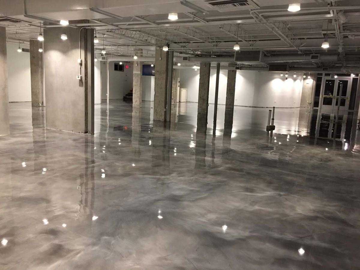 Glossy gray epoxy floor in a large, empty commercial space, reflecting overhead lights and columns.