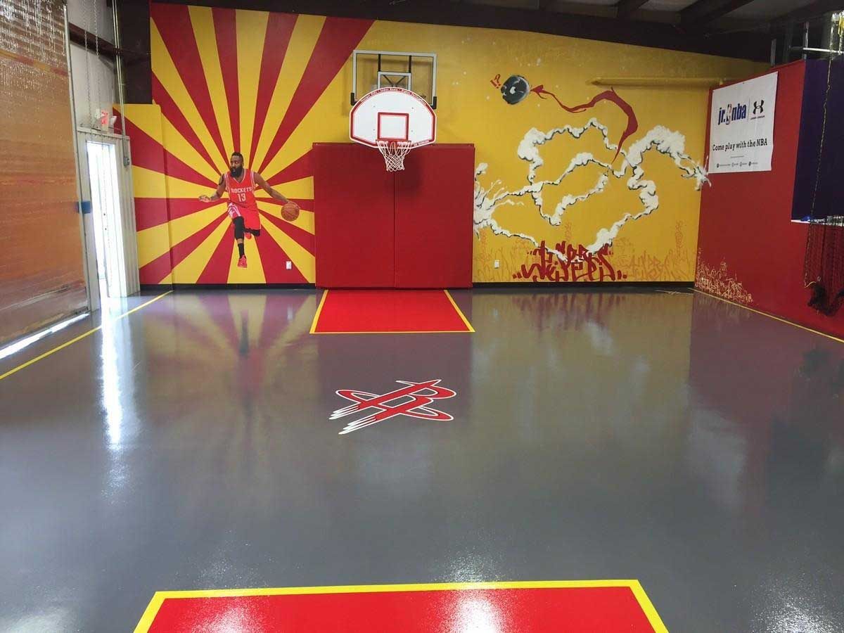 Basketball court with a red and yellow painted wall, a hoop, and a reflective gray floor.