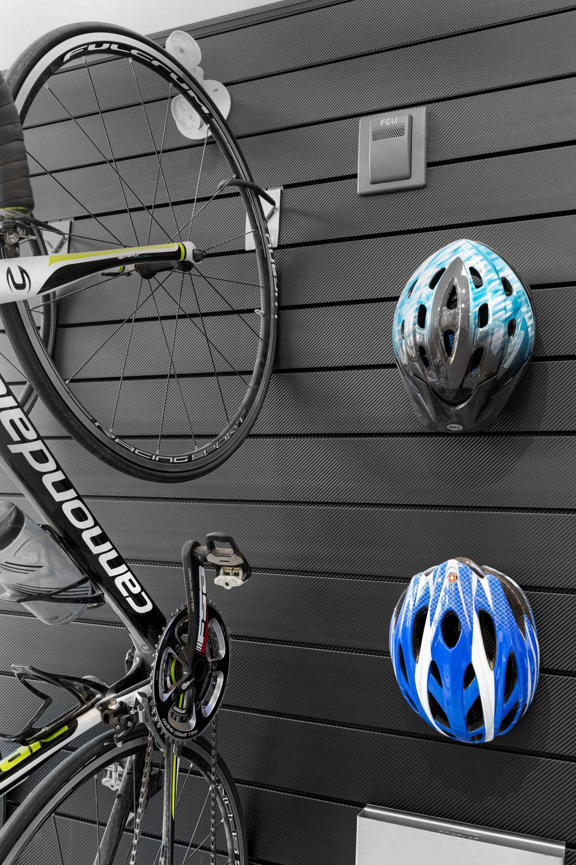 Black bike on display, with blue and black helmets mounted on a slotted wall.