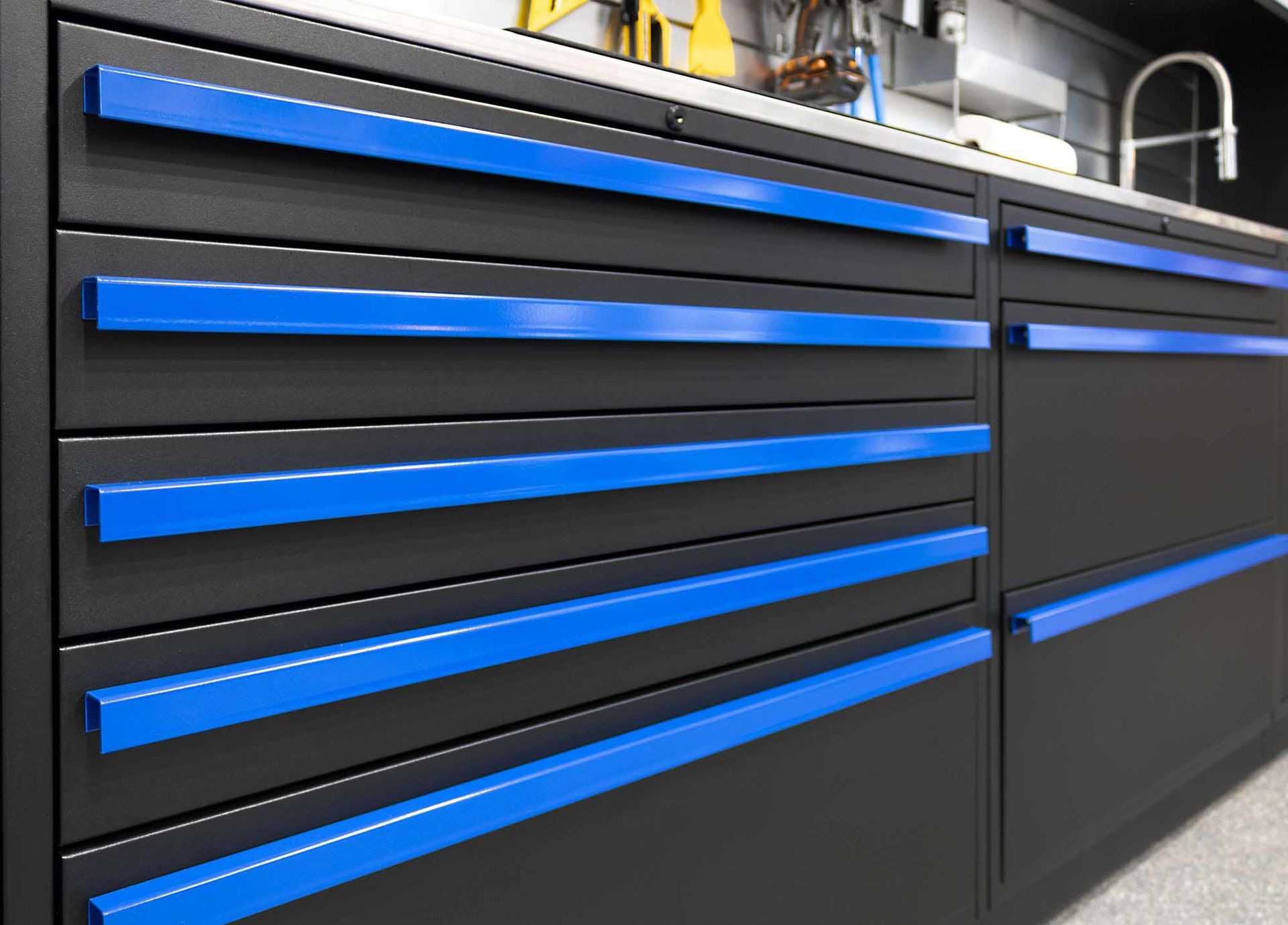 Black tool cabinet with blue drawer handles in a workshop.