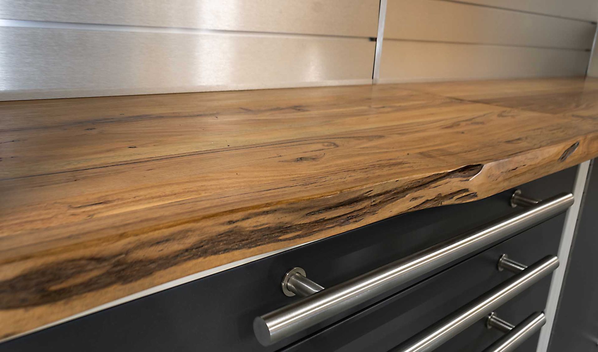 Wooden countertop with metal pulls above dark cabinets and a stainless steel backsplash.