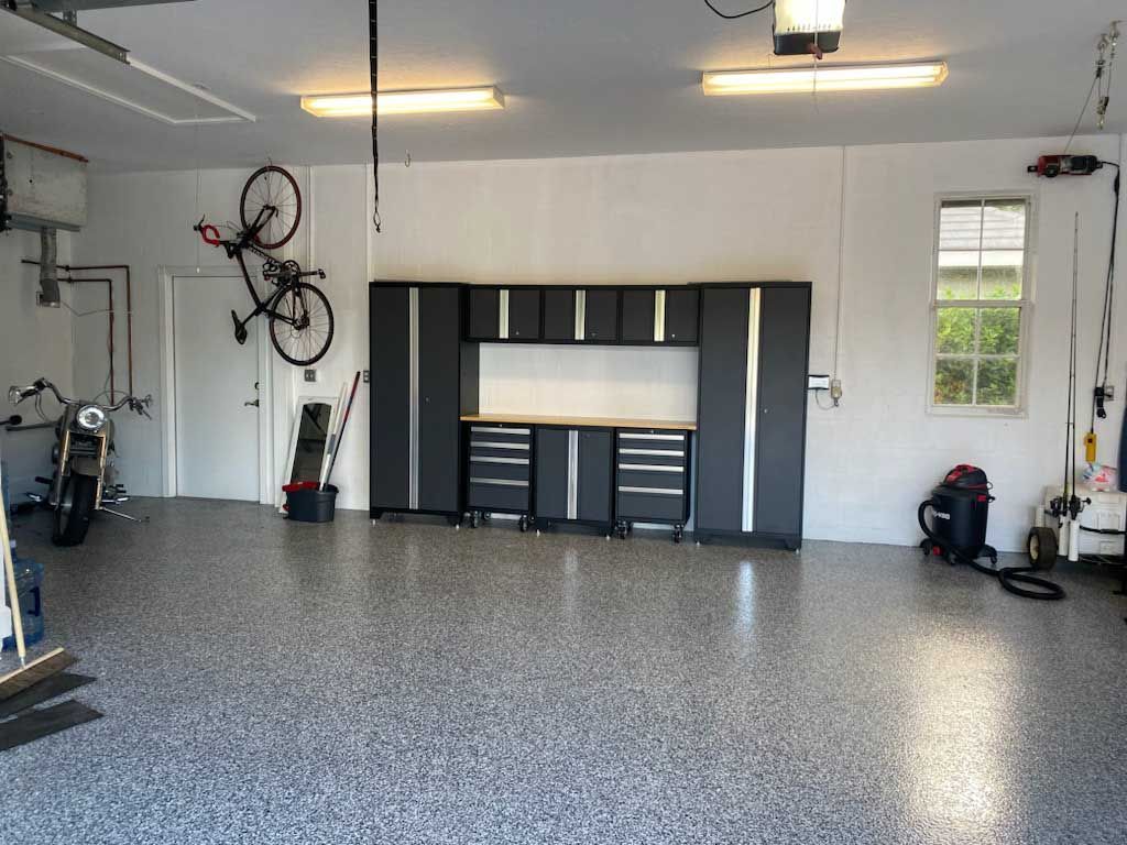 Garage interior with a motorcycle, bike, and cabinets. Grey speckled floor, white walls, and a workbench.
