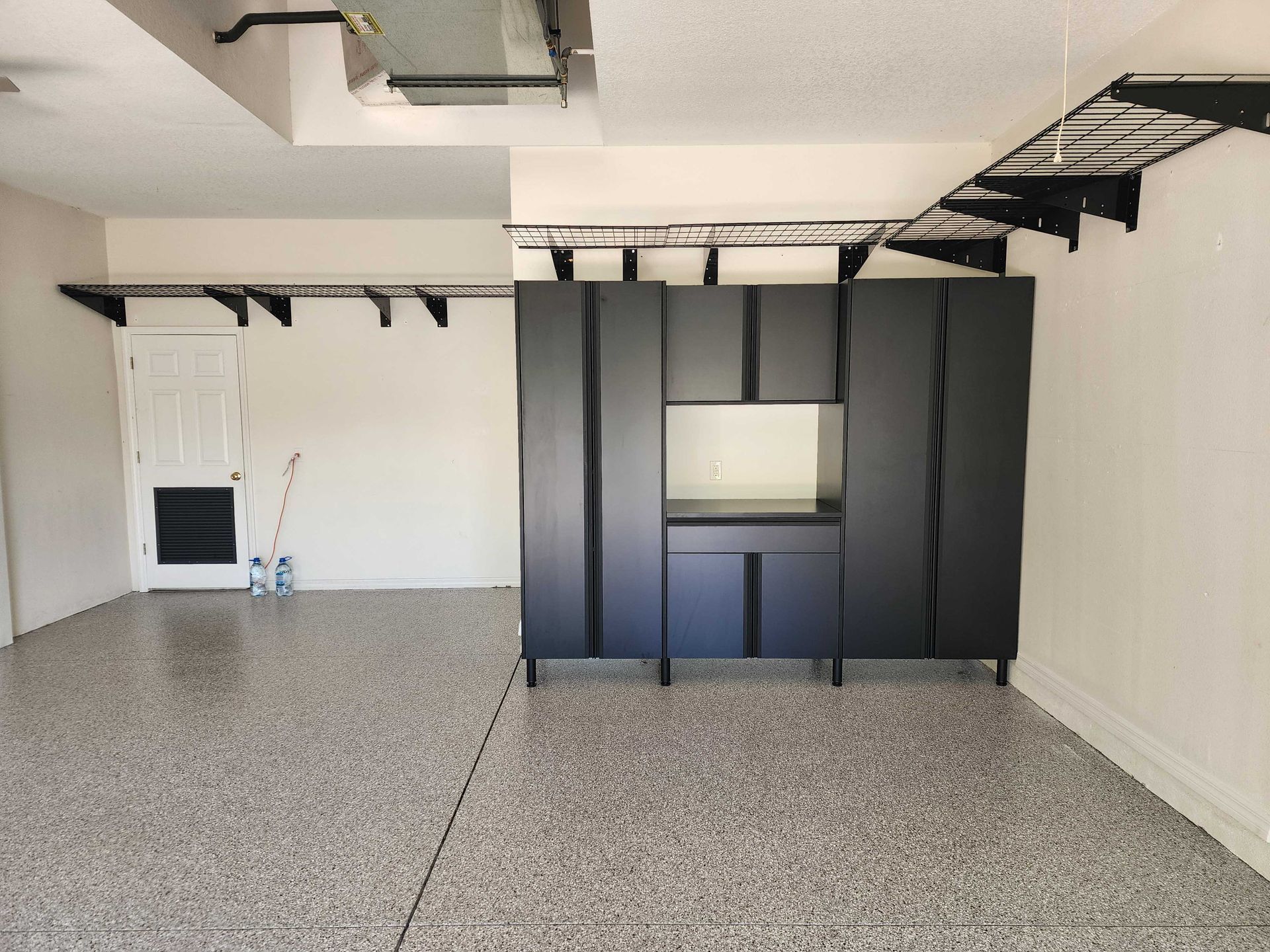 Garage with gray speckled floor, white walls, black cabinets, and shelving.