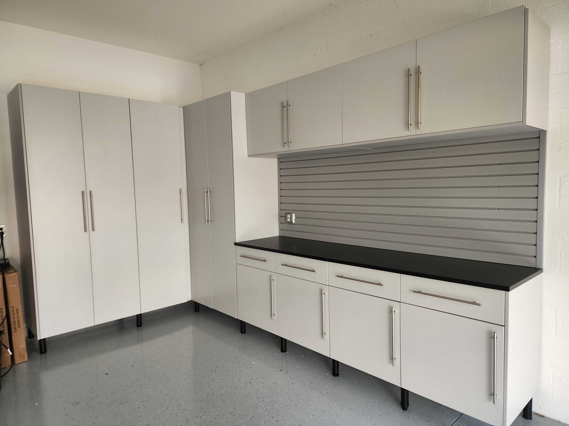 White garage storage cabinets with black countertop and gray slatted wall.