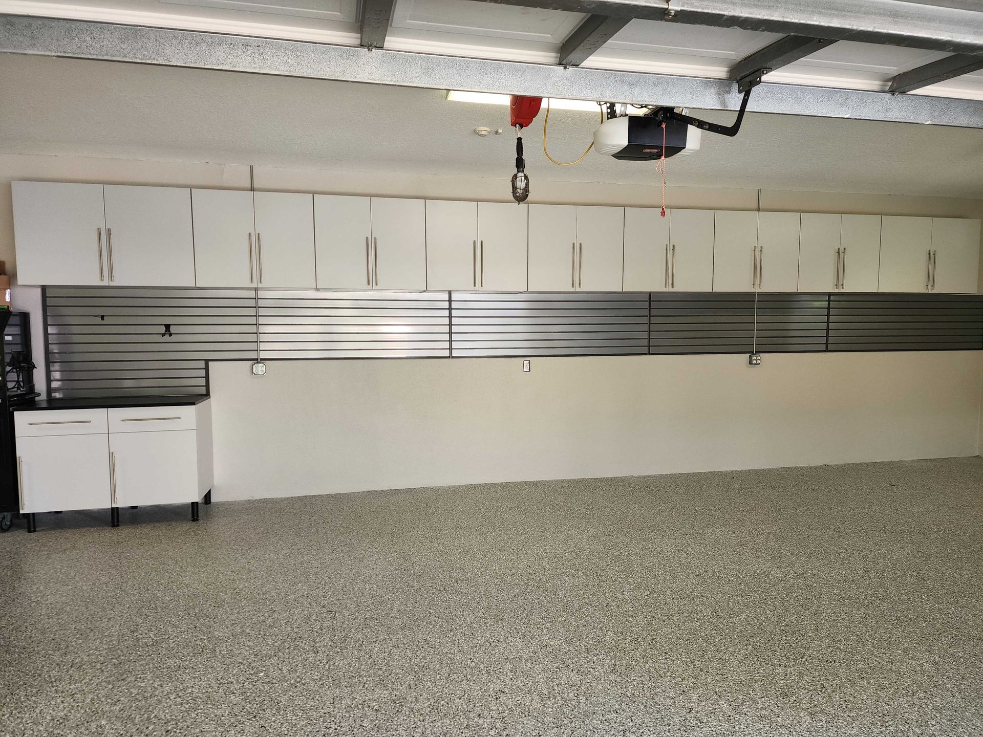 Garage with white cabinets above and below a metal rail system, epoxy floor.