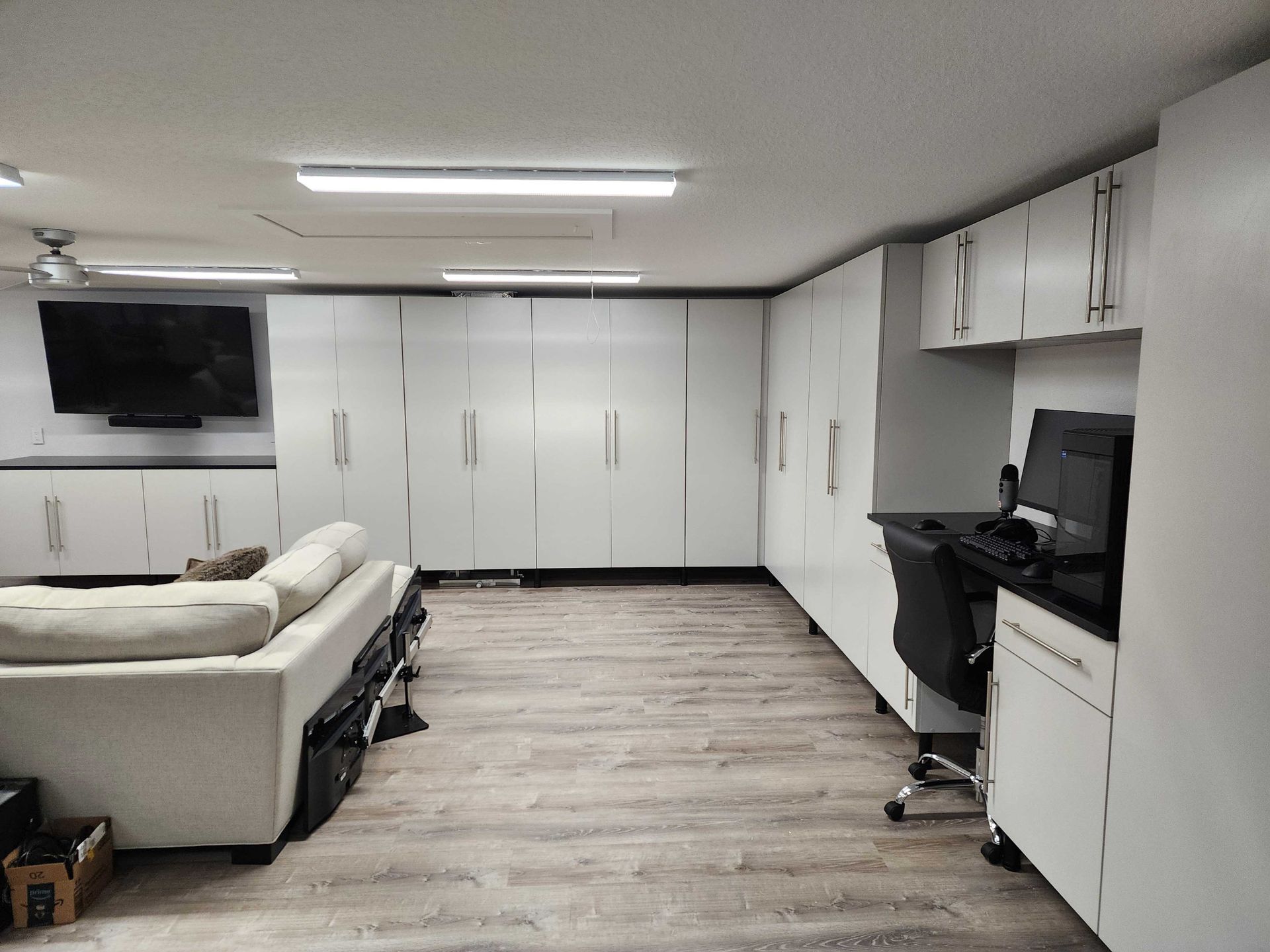 White cabinets line a room with a sofa, TV, and desk. Fluorescent lights illuminate the space.