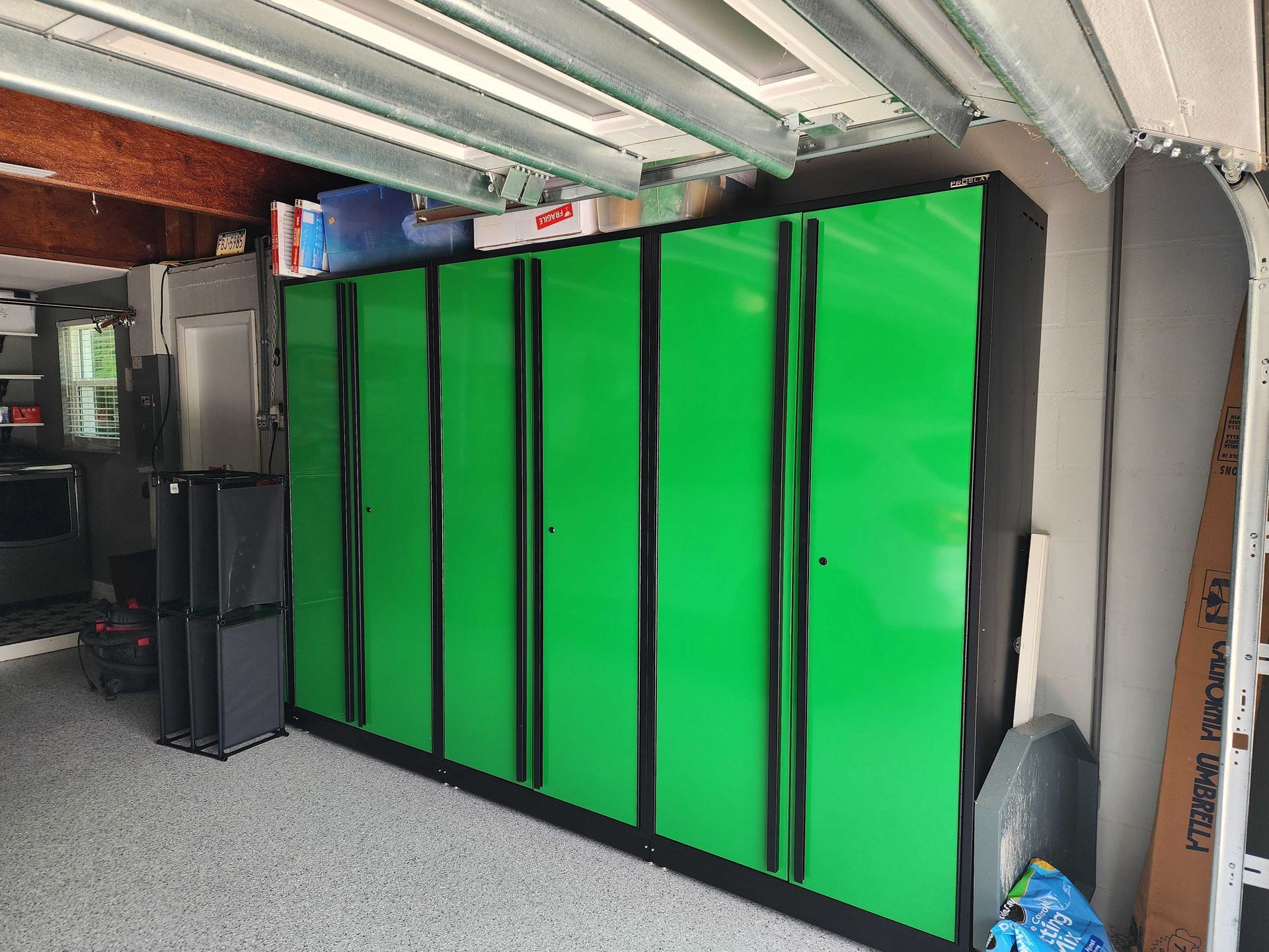 Green and black storage cabinets inside a garage with speckled flooring.