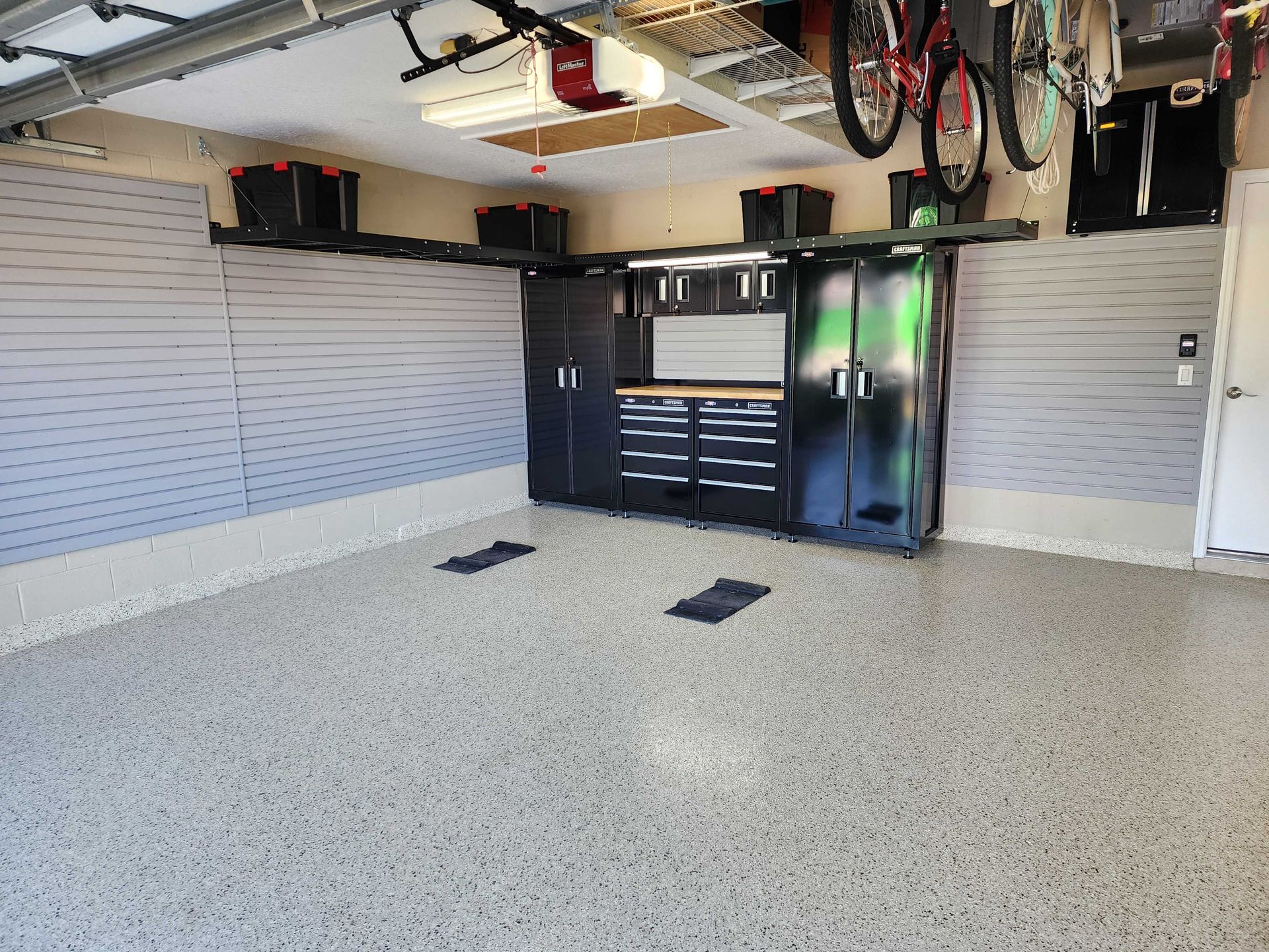 Garage interior with organized storage cabinets, workbench, and overhead racks. Gray epoxy floor, gray slat walls.