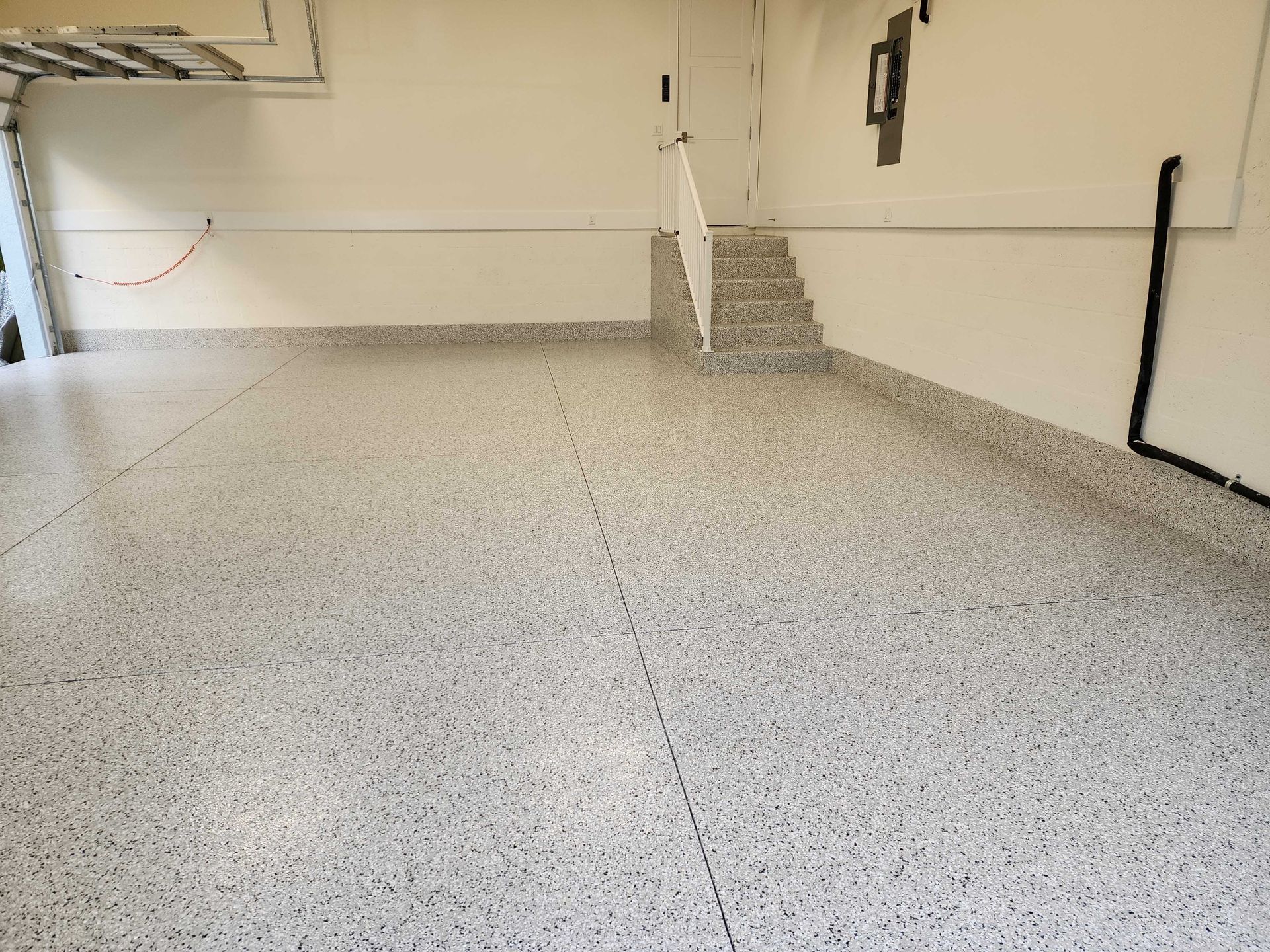 A spacious garage with a speckled epoxy floor and stairs leading up.