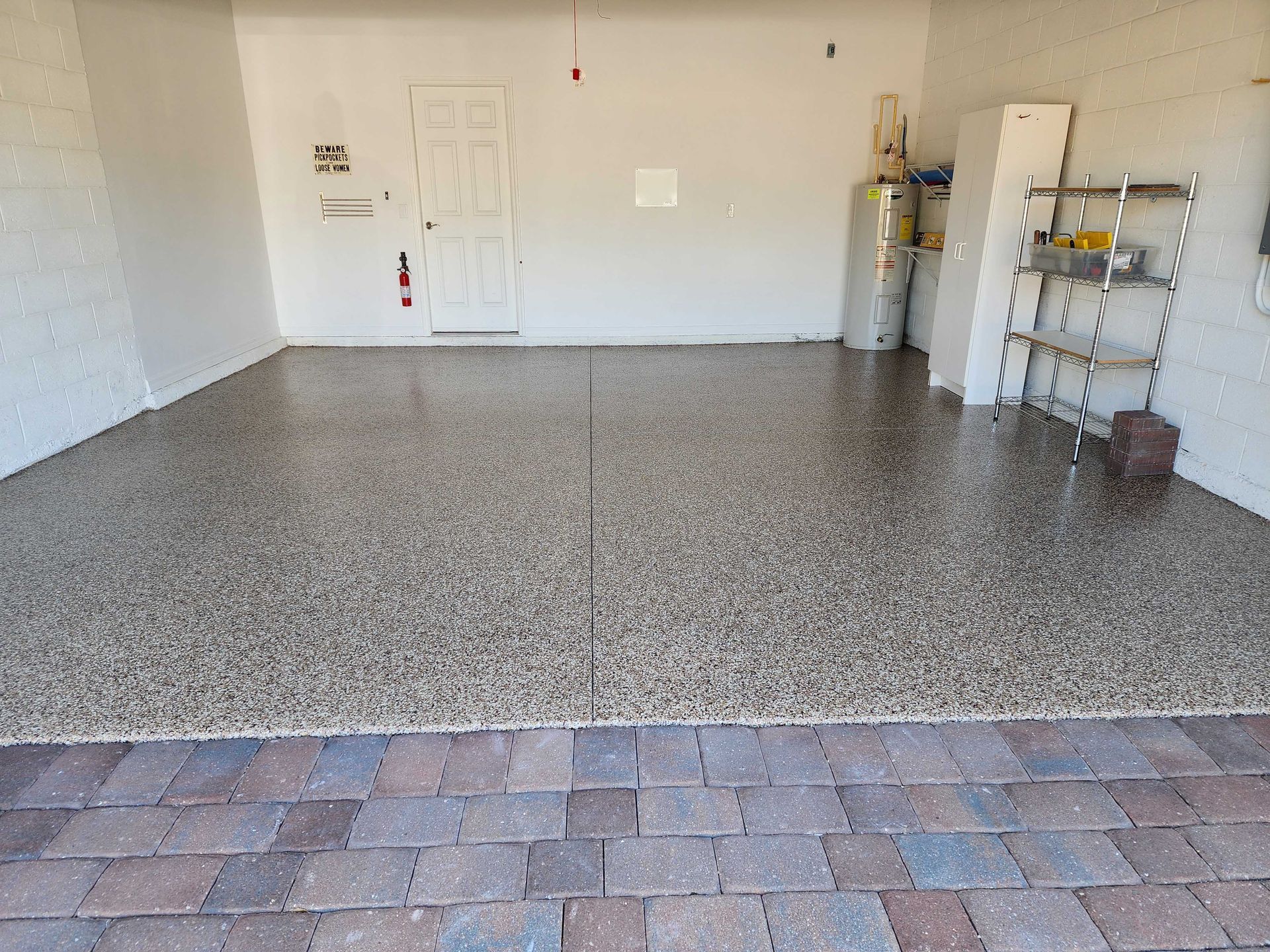 Garage with speckled epoxy floor, a brick border, and a white door in the back.