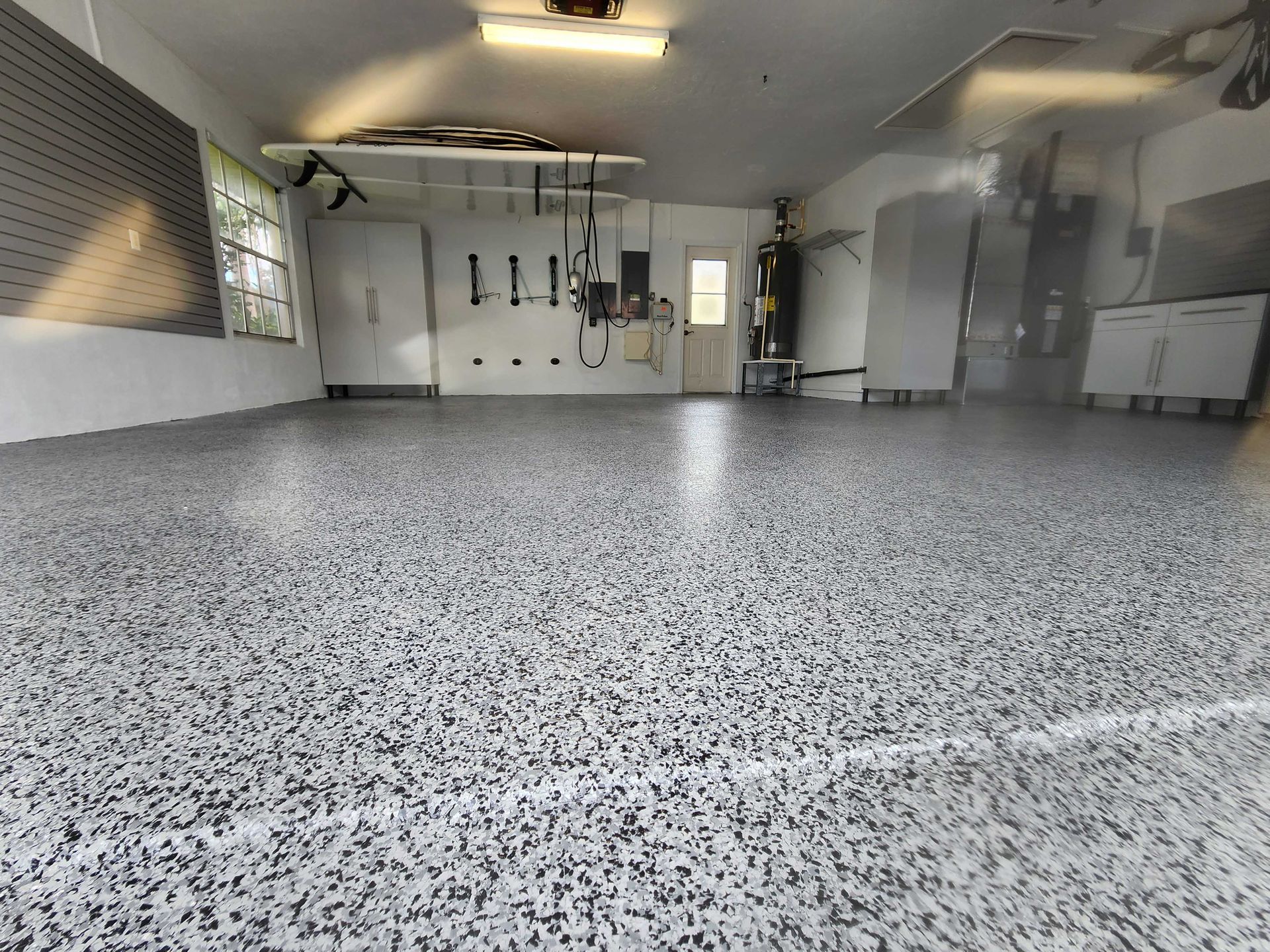 Garage with a speckled gray floor, cabinets, tools on wall.