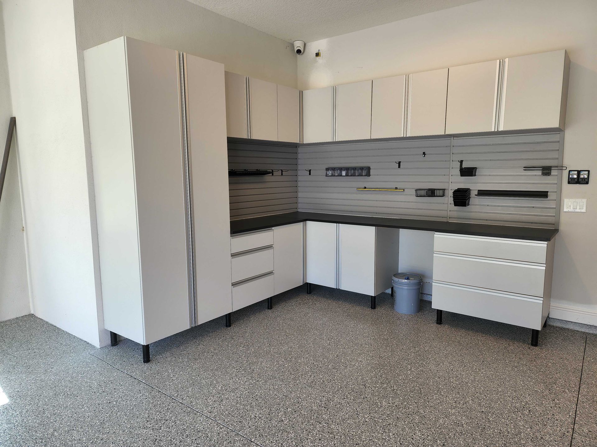 White garage storage cabinets with a gray pegboard and speckled floor.