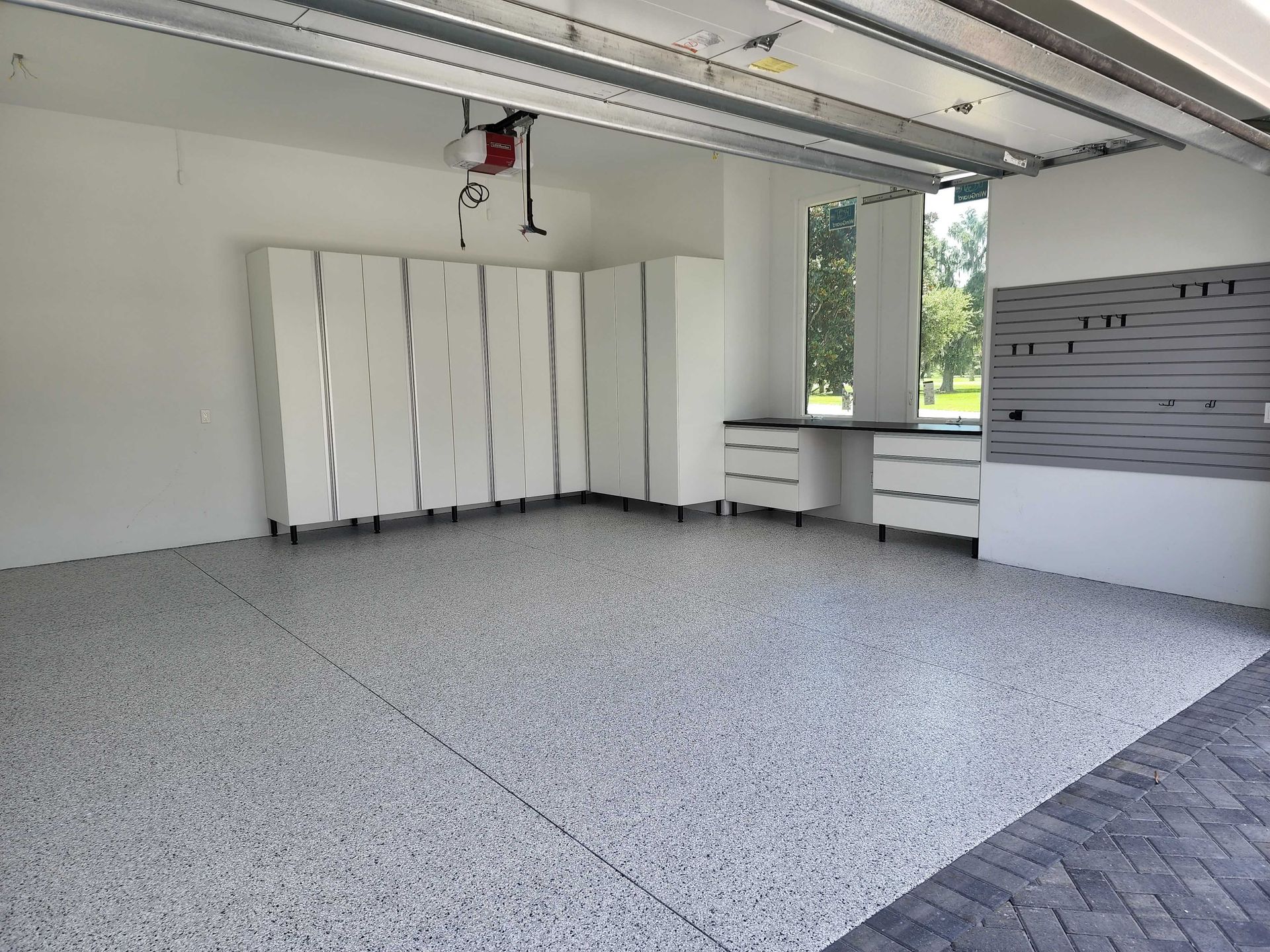 Empty, clean garage with white cabinets, speckled flooring, and a view of the outdoors.