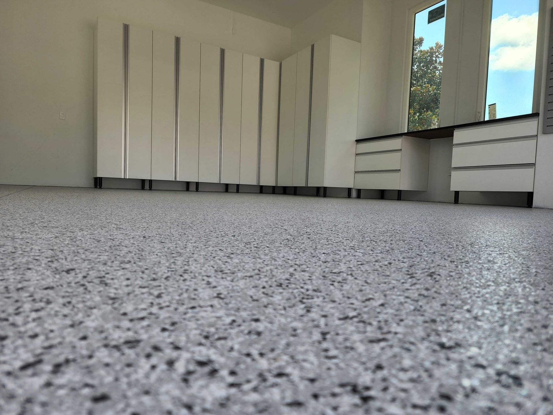 Close-up of a speckled gray floor in a room with white cabinets and a window.