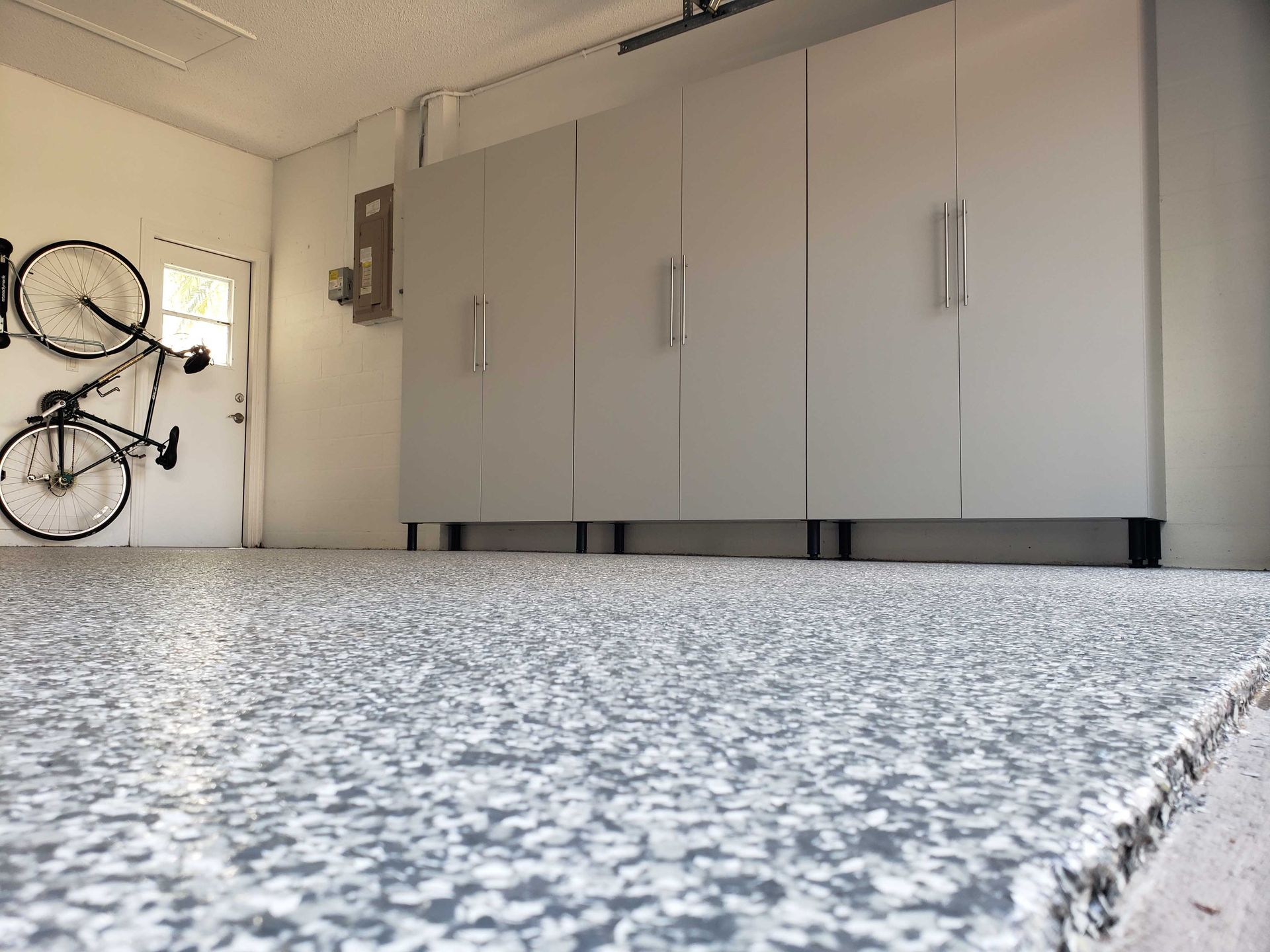 Garage with speckled gray floor, light gray cabinets, and a bicycle hanging on the wall.