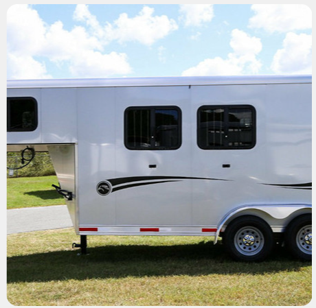 A white horse trailer is parked in a grassy field