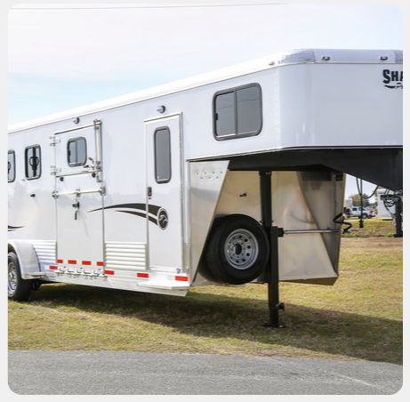 A white horse trailer is parked in a grassy field