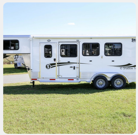 A white horse trailer is parked in a grassy field