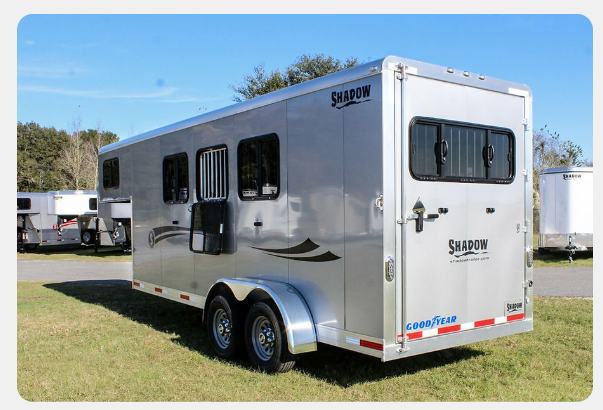 A horse trailer is parked in a grassy field.