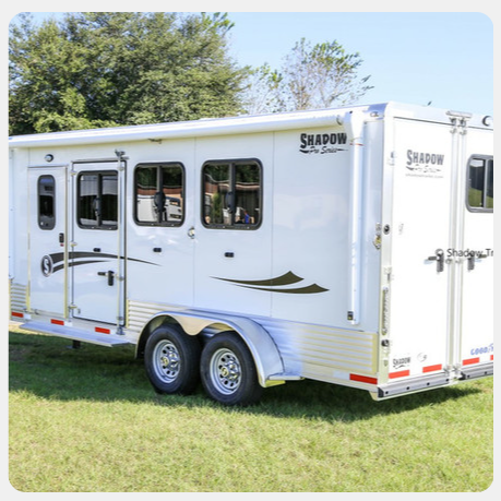 A white horse trailer is parked in a grassy field.