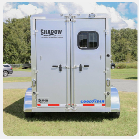 A shadow trailer is parked in a grassy field.