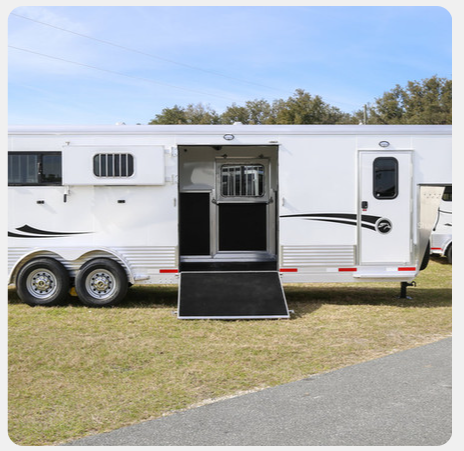 A horse trailer with the door open is parked in a grassy field.