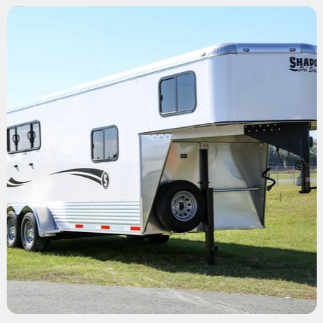 A white horse trailer is parked in a grassy field.