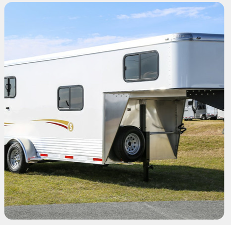 A white horse trailer is parked in a grassy field