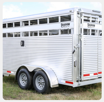 A silver horse trailer is parked in a grassy field.