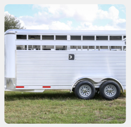 A white horse trailer is parked in a grassy field.