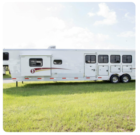 A horse trailer is parked in a grassy field.