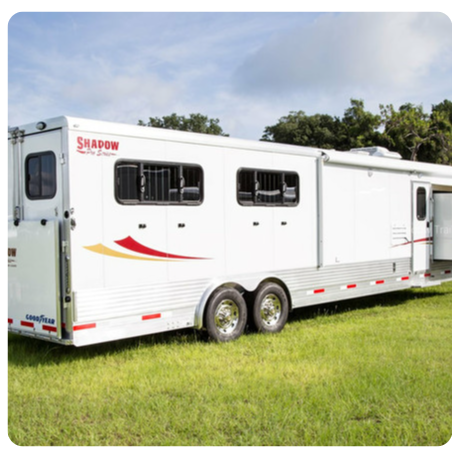 A white shadow trailer is parked in a grassy field
