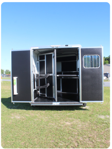 A black trailer with the doors open is parked in a grassy field