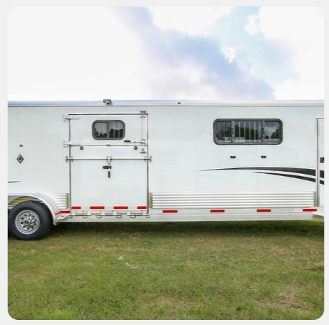 A white horse trailer is parked in a grassy field