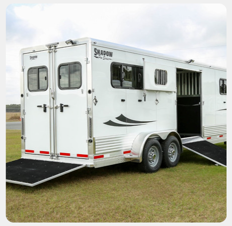 A white horse trailer is parked in a grassy field.