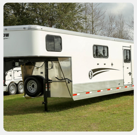 A white horse trailer is parked in a grassy field