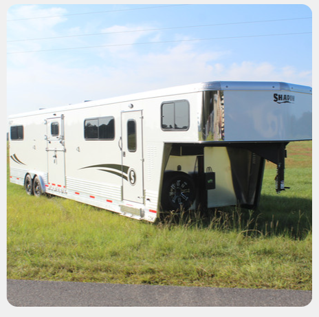 A white horse trailer is parked in a grassy field