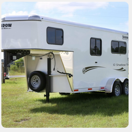 A white horse trailer is parked in a grassy field