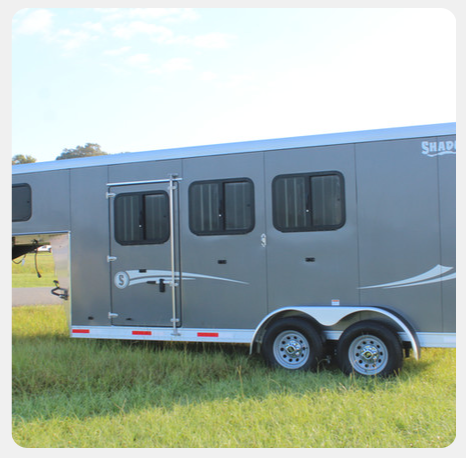 A horse trailer is parked in a grassy field