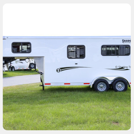 A white horse trailer is parked in a grassy field.