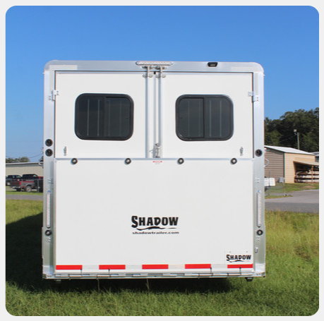 A white trailer with shadow written on the side is parked in a grassy field.