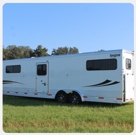 A white horse trailer is parked in a grassy field