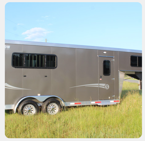 A horse trailer is parked in a grassy field